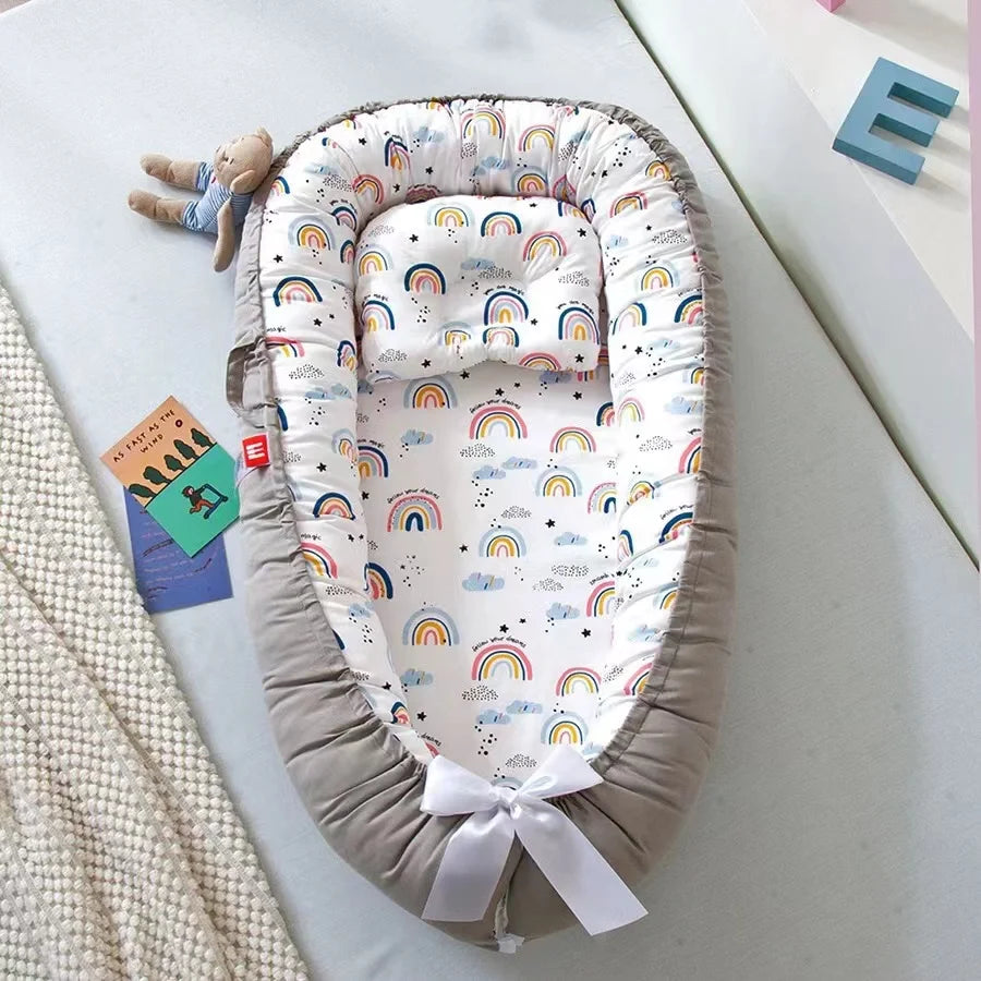 Un Lit de Bébé Portable douillet | Le Cocon Parfait un Sommeil Paisible de BABY-PREMA au joyeux motif arc-en-ciel, accompagné d'une peluche et d'un livre d'histoires ludique, prêt pour l'aventure dodo des petits.