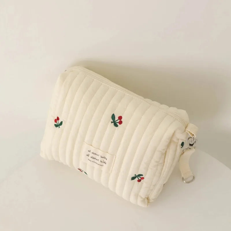 Un Sac à Couches en Coton pour poussette doux et matelassé de couleur ivoire, orné de petits motifs de cerises rouges et vertes et d'un délicat texte écrit, parfait pour les essentiels de maternité pour enfants de BABY PREMA.