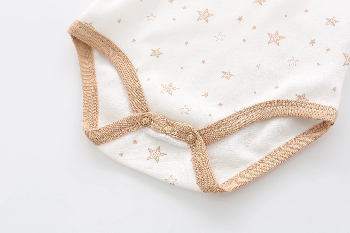 Image en gros plan d'une combinaison blanche pour bébé avec des motifs d'étoiles beiges, avec une bordure beige et trois boutons-pression en bas. Confectionné en matière respirante, ce Lot de 5 Bodys Coton Agréables & conforts de BABY PREMA assure à la fois douceur et confort à votre tout-petit.