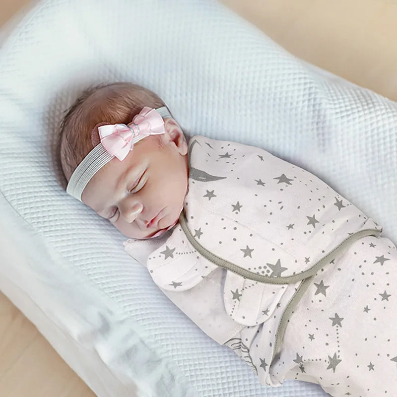 Un nouveau-né paisible endormi, emmailloté dans une couverture à motif étoilé BABY PREMA et portant un bandeau à nœud rose tendre.
