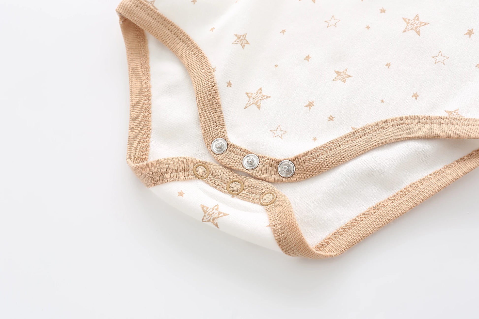 Gros plan sur une combinaison bébé blanche avec bordure marron et motifs étoiles, confectionnée en matière respirante. Ce Lot de 5 Bodys Coton Agréables & conforts de BABY PREMA comporte trois boutons pression en bas pour une fermeture facile, assurant douceur et confort à votre tout-petit.