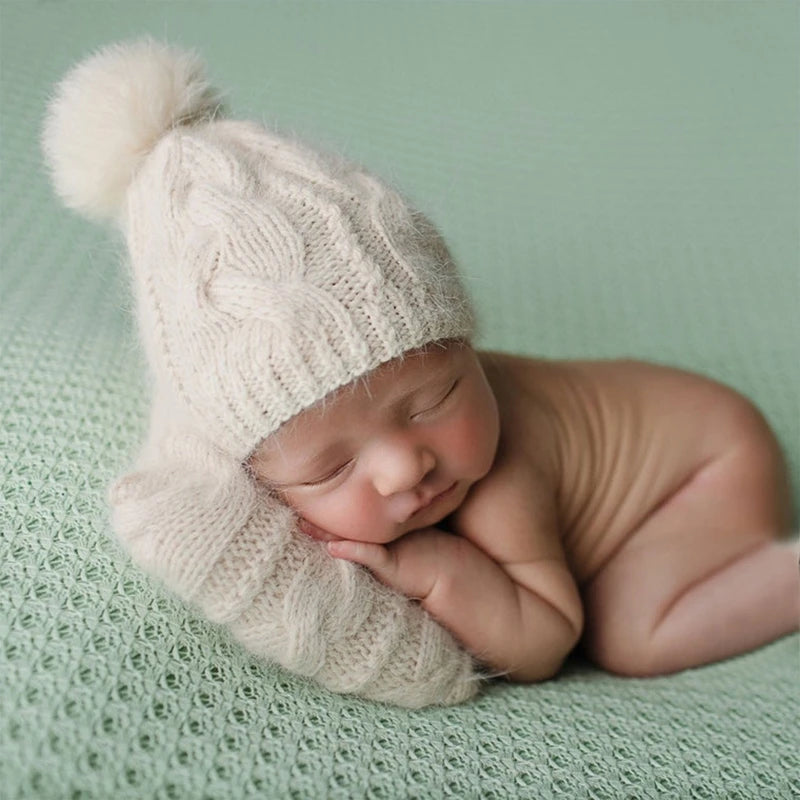 Un nouveau-né au sommeil paisible, portant un bonnet tricoté douillet à plume BABY PREMA, confortablement niché sur un textile vert doux du Set Cadeau Naissance Bébé | 2 pièces pour Bébé.