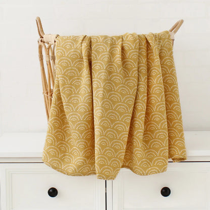 Rideau jaune doré à motif festonné suspendu à une tringle en bois au-dessus d'un meuble blanc, accessoirisé avec les accessoires BABY PREMA Couverture Bébé en Coton et Bambou Bio.