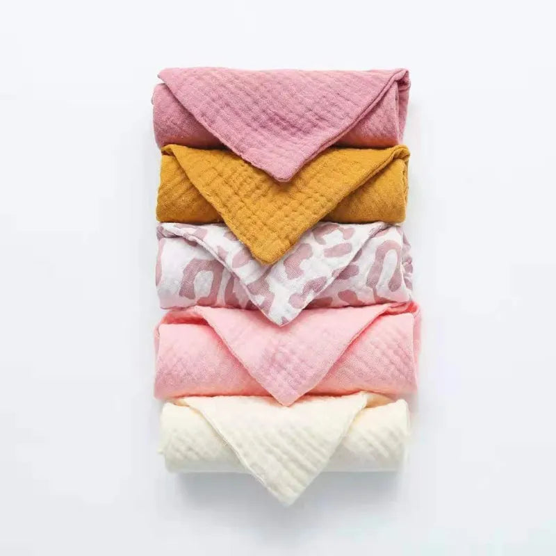 Une collection soigneusement empilée de Lot de 5 Langes Bébé en Coton de BABY PREMA dans une variété de couleurs et de textures, dont le rose, la moutarde et le blanc avec un motif à motifs, parfait pour le dodo de bébé.