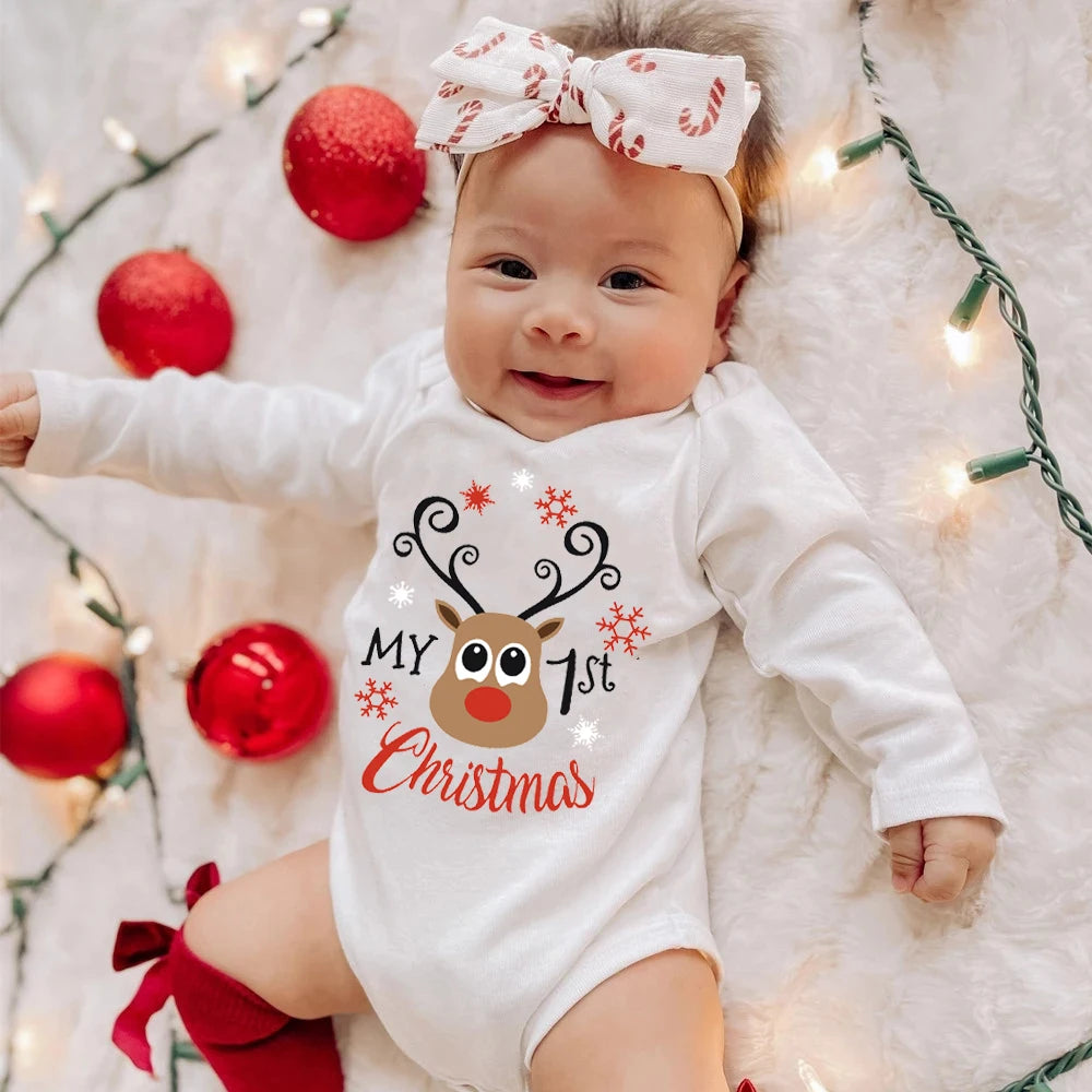 Un bébé portant une combinaison festive « Mon 1er Noël » avec un motif de renne repose sur une douce couverture blanche. Cet adorable Body Coton Noel 2024 Bébé de BABY-PREMA est complété par un noeud orné de motifs de cannes de bonbon, entouré d'ornements rouges et de lumières de Noël.