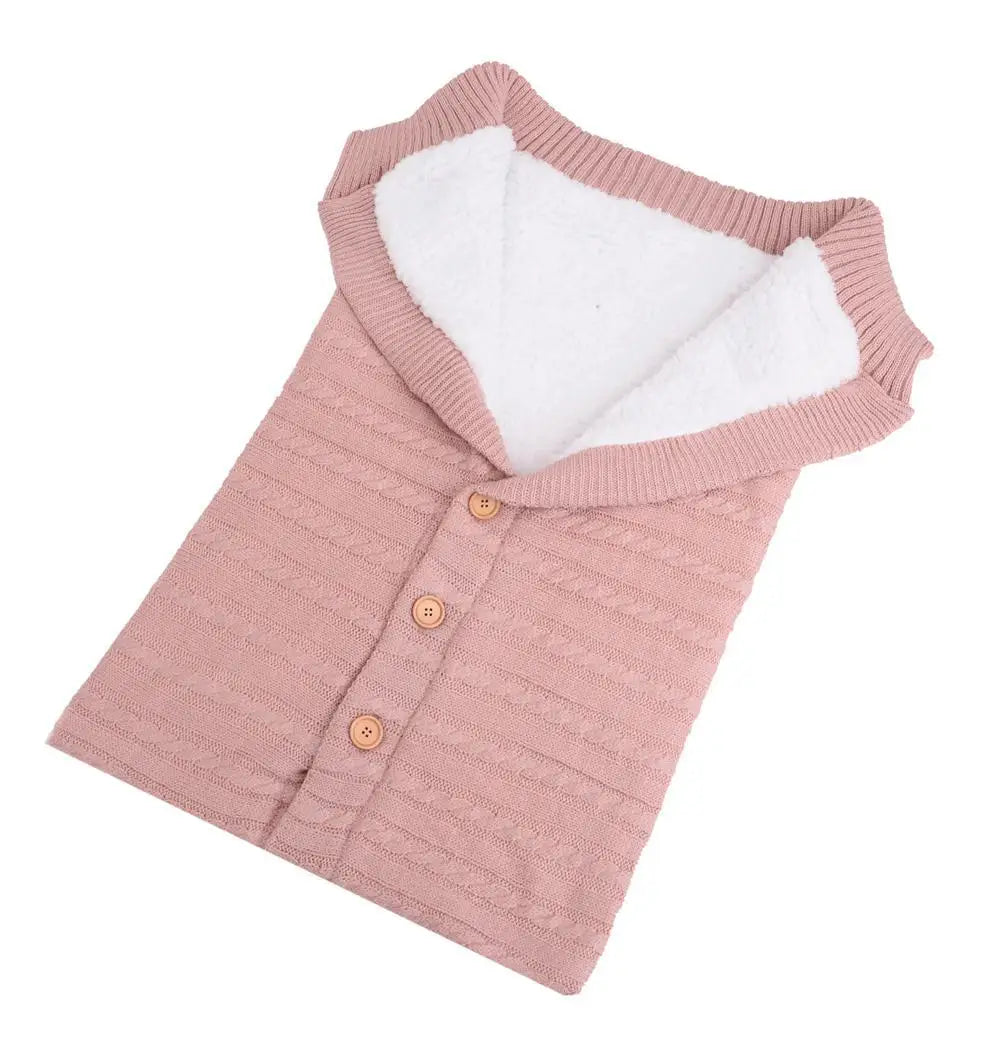 Un pull bébé tricoté rose douillet avec une doublure duveteuse blanche et des boutons en bois, disposé à plat sur un fond blanc, la Couverture en Polaire Ultra Doux et Moelleux de BABY PREMA.