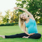 Une femme enceinte souriant et s'étirant lors d'une séance de yoga dans un parc verdoyant portant le Legging de Grossesse Taille Haute de Baby Prema.