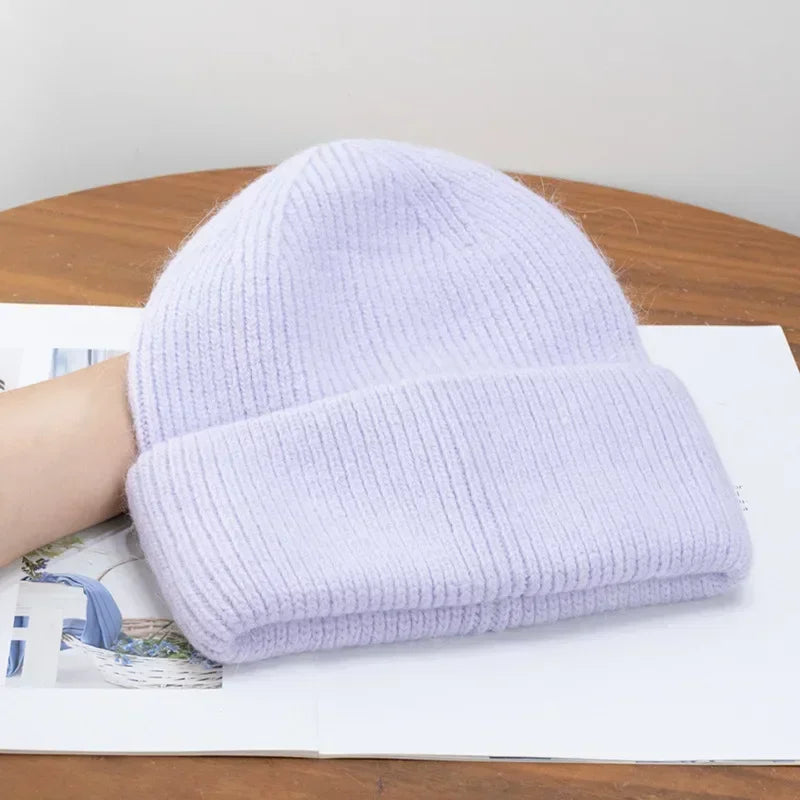 Un bonnet angora pour maman de couleur lilas reposant sur une table en bois avec un peu de matériel imprimé visible en dessous.