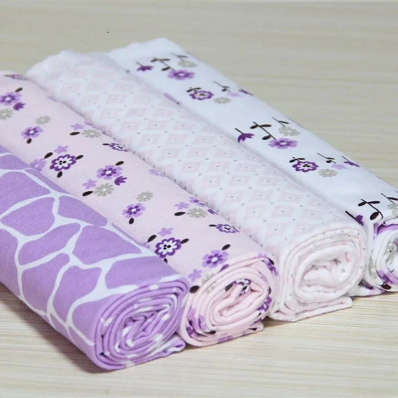 Un ensemble de Lot de 4 Carré de Langes soigneusement pliés et roulés aux motifs violets et blancs de BABY PREMA, présentant une variété de motifs, notamment des fleurs et des formes géométriques, parfaits pour le dodo d'un bébé.