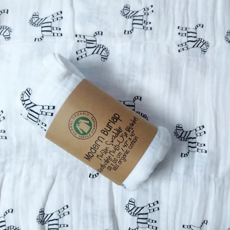 Un rouleau de Couverture en Mousseline de Coton pour Bébé biodégradable et biologique sur une surface en tissu à motif zébré, parfait pour BABY PREMA.