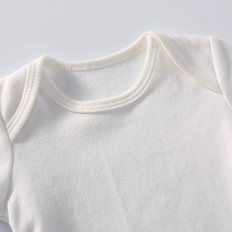 Une vue rapprochée d'un bébé blanc sur un fond blanc. Le Body coton Manches Longues de BABY-PREMA présente une encolure ronde avec des coutures renforcées et des rabats d'épaules superposés pour un enfilage facile. Le tissu semble doux et confortable, adapté à un nourrisson.