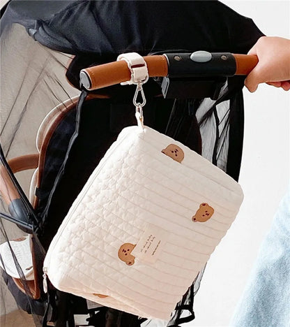 Une personne tenant le guidon d'un scooter avec un sac de rangement bébé BABY PREMA orné de jolis motifs d'ours suspendus à un crochet, parfait pour transporter les essentiels légers de mon bébé.