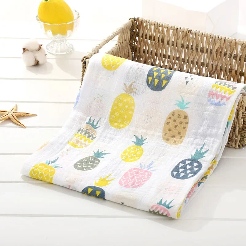 Un torchon de cuisine coloré avec des motifs d'ananas drapé sur le bord d'un panier en osier sur une surface en bois blanc, créant une ambiance estivale joyeuse et fraîche pour les Langes en Mousseline en Coton pour Bébé de BABY PREMA.