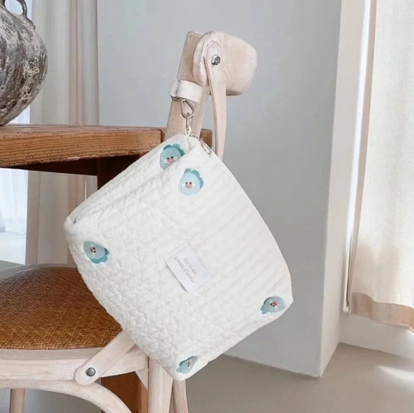 Un sac à main tendance Sac de Couches Rangement Bébé orné d'accents floraux colorés suspendus nonchalamment à une chaise en bois, dégageant une ambiance d'élégance décontractée par BABY PREMA.