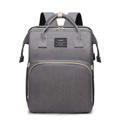 Un élégant Sac à Langer 3 en 1 Pour Maman & Bébé gris de BABY-PREMA, avec des fermetures éclair dorées, une poignée supérieure et des bretelles, sur un fond blanc. Il est conçu pour le petit enfant, alliant élégance et praticité.