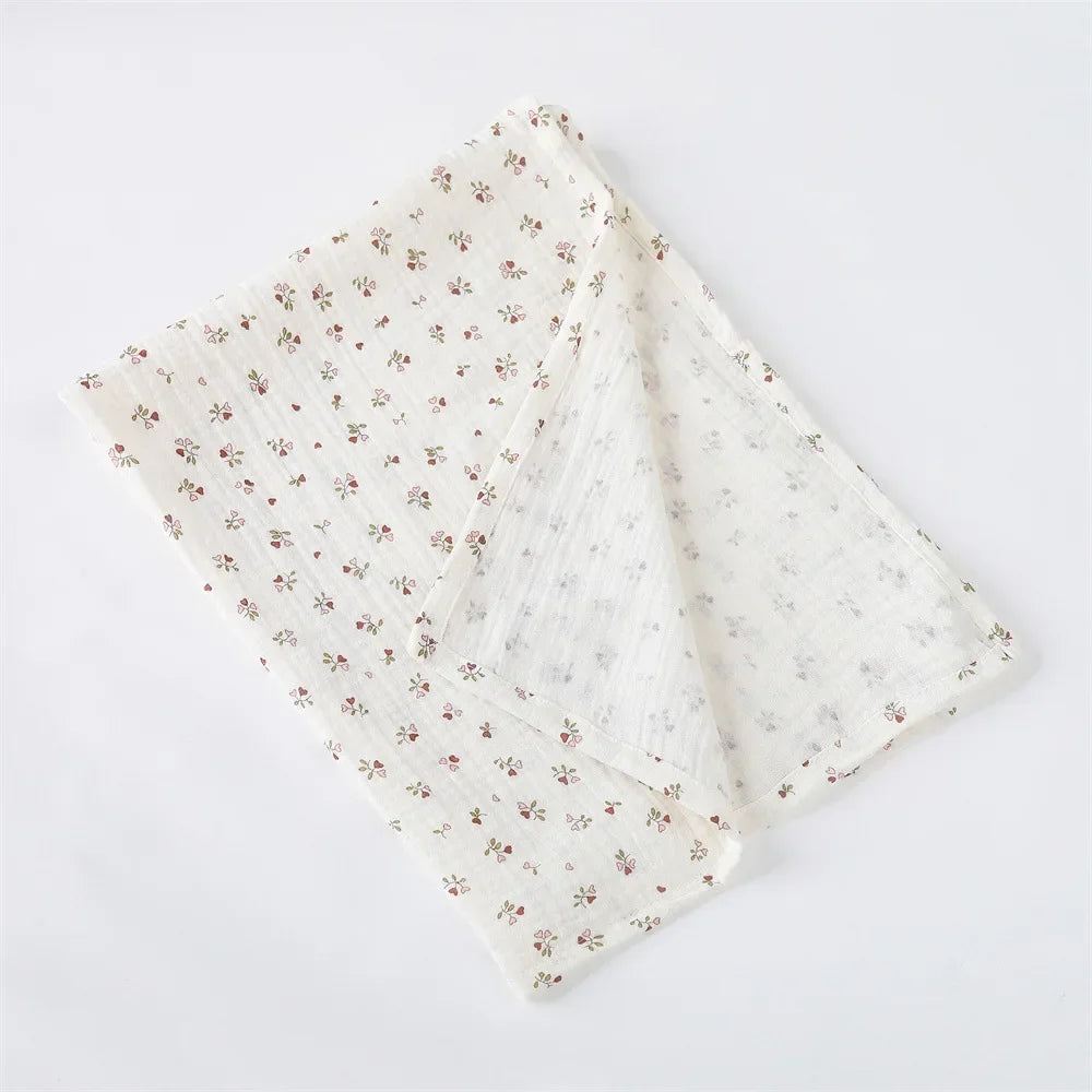 Un tissu fleuri plié aux teintes douces, accessoire indispensable pour bébé, posé sur un fond blanc réalisé par Couverture Emmaillotage en coton pour Bébé de BABY PREMA.