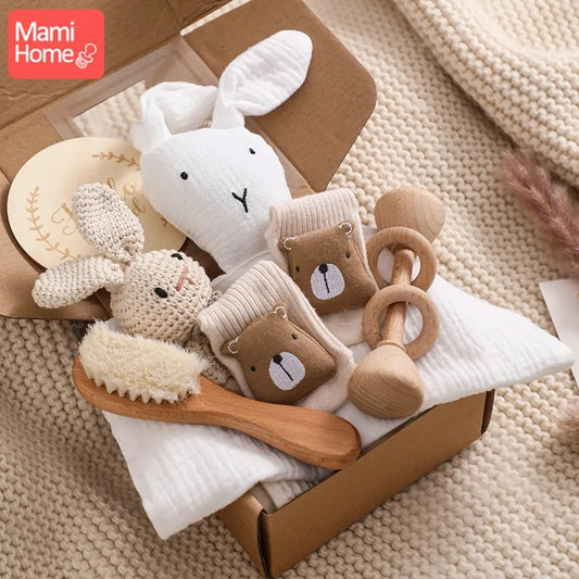 Une sélection chaleureuse de jouets pour bébé faits à la main et du Coffret Cadeau Naissance Bébé de BABY PREMA, comprenant un anneau de dentition en bois, un ours en peluche et des oreilles de lapin douces, judicieusement disposés dans un coffret cadeau.