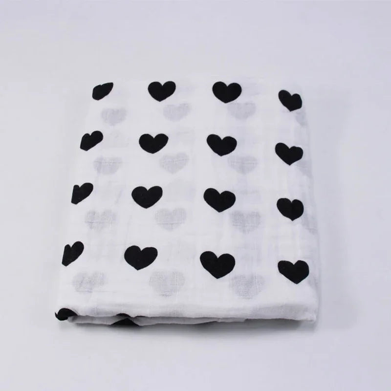 Tissu blanc à motif de coeurs noirs, Couverture en Mousseline de Coton pour Bébé de BABY PREMA, soigneusement plié sur fond uni.
