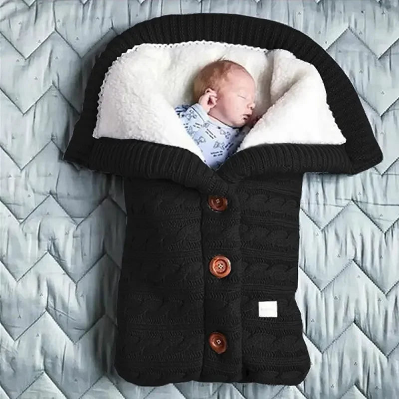 Nouveau-né dormant paisiblement dans une douillette couverture de poussette pour bébé BABY PREMA, entourée d'accessoires bébé doux, sur un fond à motifs.