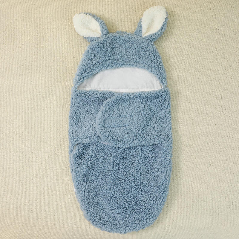 Un Cocon Couverture bébé bleu douillet avec des oreilles de lapin attachées à la capuche, affichées sur un fond de couleur claire, est un accessoire bébé indispensable de BABY PREMA.