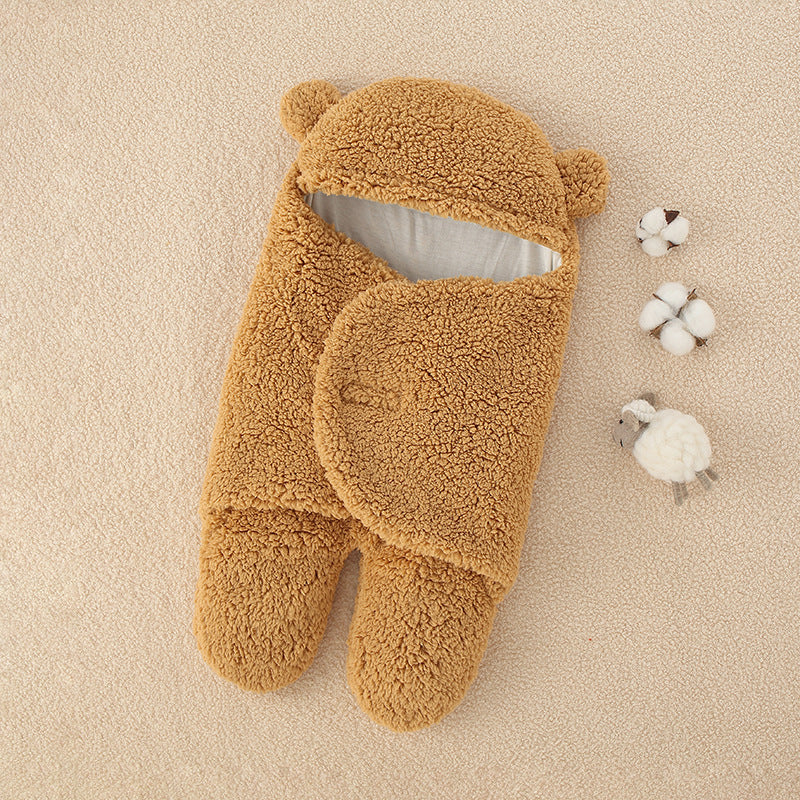 Une paire de chaussons douillets Couverture épaisse douce bébé de BABY PREMA sur un fond doux et sableux, accompagnée de décorations végétales en coton et d'accessoires bébé.