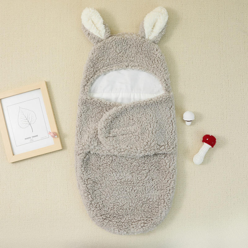 Un Cocon Couverture bébé douillet avec un motif d'oreilles de lapin, à côté d'un petit jouet et d'un cadre photo, disposés sur une surface douce. Cet article bébé BABY PREMA est parfait pour assurer le confort de votre tout-petit.