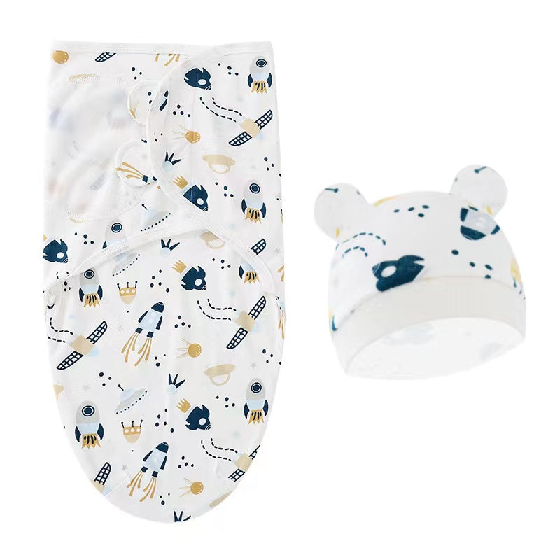 Une adorable couverture d'emmaillotage blanche BABY PREMA avec un motif fantaisiste de couronnes, d'étoiles et de formes ludiques, associée à un joli bonnet assorti avec des accents d'oreilles, parfait pour un ensemble confortable et élégant.