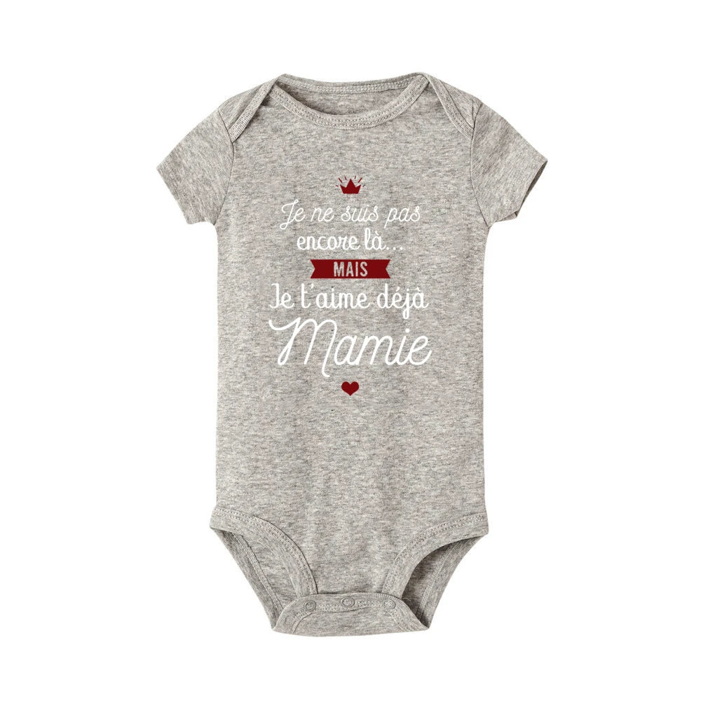 Un Body Coton été Imprimé gris pour un enfant en bas âge, avec un texte blanc et rouge qui dit : "Je ne suis pas encore là... MAIS je t'aime déjà Mamie", accompagné d'un petit cœur rouge et d'un motif couronne. . Parfait comme cadeau grand-mère ! Il s'agit de la marque BABY-PREMA.