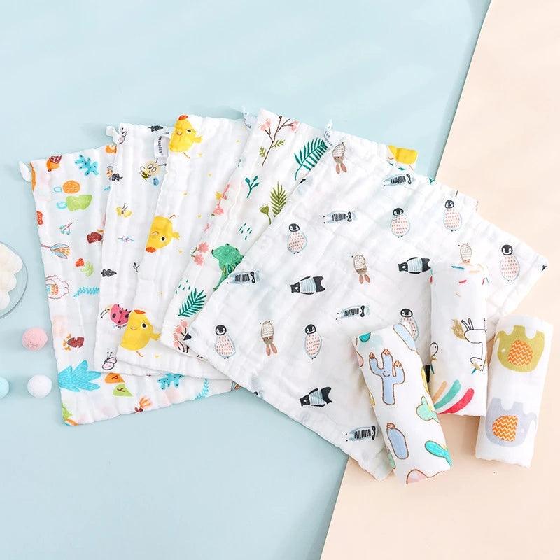 Une gamme colorée de 5 Langes Coton Mousseline pour Bébé de la marque BABY-PREMA, aux divers motifs mignons, nécessaires pour l'hygiène bébé, disposées sur une surface bleu pâle.