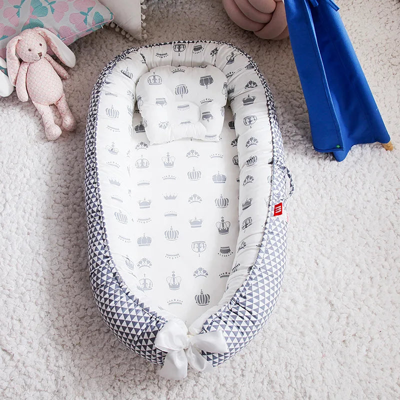 Un Nid de Cocoon portable Lit de Bébé douillet de BABY-PREMA avec un motif géométrique niché sur un tapis moelleux, flanqué d'un lapin en peluche rose tendre et d'une couverture bleue, créant un endroit serein et invitant pour un tout-petit