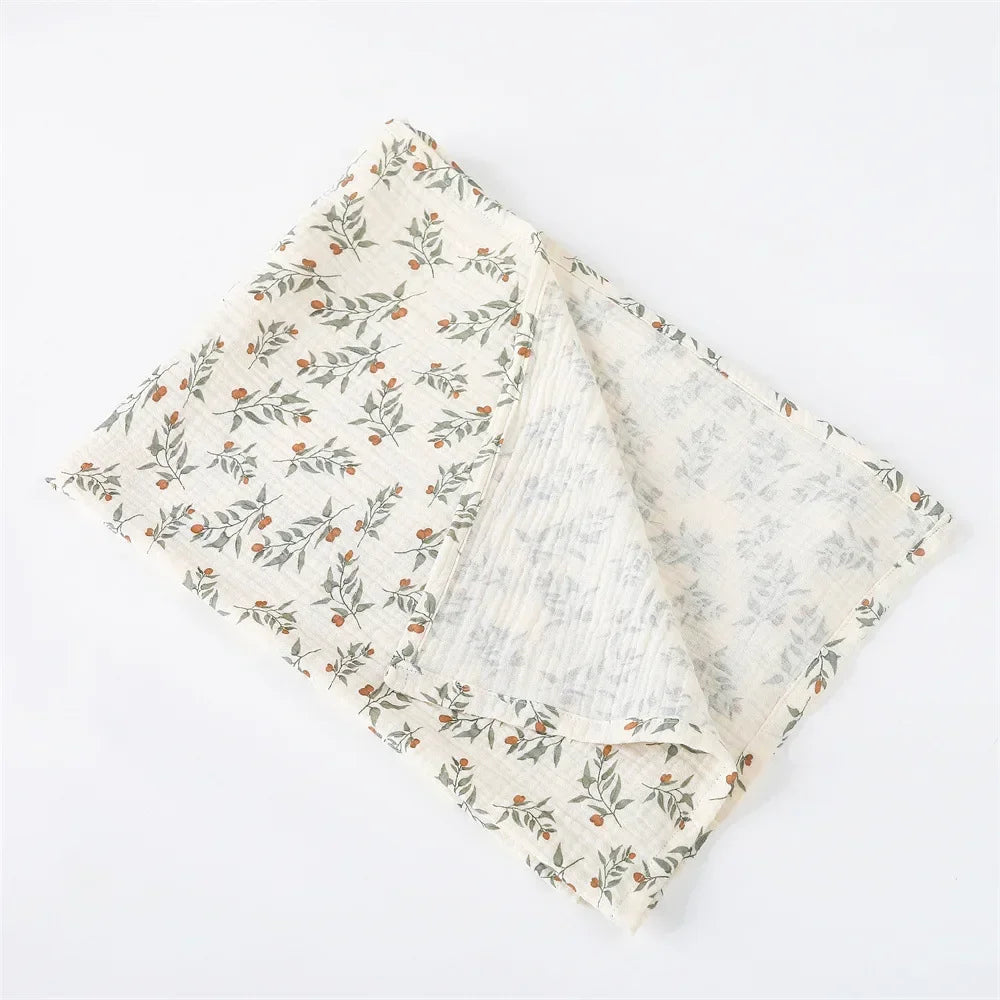 Une Couverture Emmaillotage en coton soigneusement pliée avec un motif floral et feuillu sur fond blanc, parfaite comme accessoire d'hygiène pour bébé de BABY PREMA.