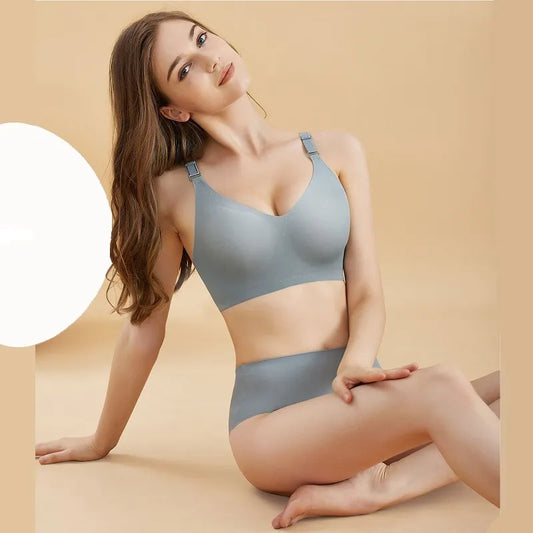 Une femme posant dans un soutien-gorge de sport gris BABY PREMA confortable et un bas assorti, assise sur un fond beige chaud avec une douce lueur blanche à ses côtés, sa petite silhouette accentuée dans le tissu léger.