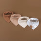 Un lot de 4 bavoirs en mousseline de coton pour bébé BABY-PREMA dans les tons marron, beige et blanc sont exposés horizontalement sur un fond marron. Les trois premiers bavoirs en mousseline de coton BABY-PREMA sont de couleurs unies, tandis que le quatrième bavoir est blanc avec des motifs célestes, dont un soleil, une lune et des étoiles.