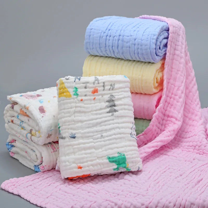 Assortiment de couvertures douces pour bébé aux couleurs pastel soigneusement pliées et empilées, avec une couverture rose confortable étalée au premier plan. Couvertures Mousseline | 6 Couches pour Nouveau-né par BABY PREMA