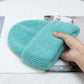 Une main tenant une peluche Bonnet Angora Pour Maman couleur aqua posée délicatement sur un article ouvert BABY PREMA.