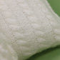 Vue rapprochée d'une texture de tissu tricoté blanc sur fond vert, parfaitement dimensionnée pour le Set Cadeau Naissance Bébé de BABY PREMA | 2 pièces pour Bébé.