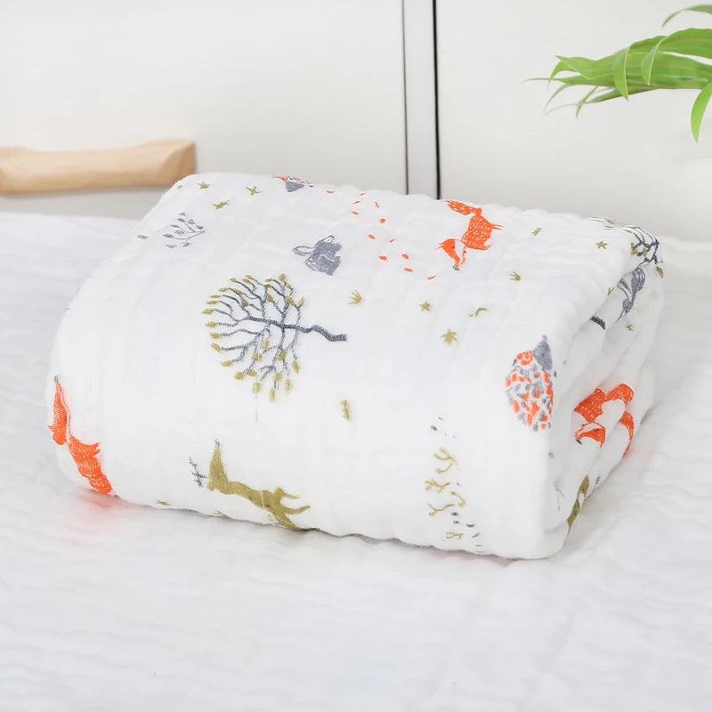 Une Couvertures Mousseline soigneusement pliée | 6 Couches pour Nouveau-né en BABY PREMA avec des imprimés colorés d'animaux et de nature, conçus comme un accessoire bébé douillet, posés sur une surface blanche avec une plante en pot en arrière-plan, offrant une ambiance chaleureuse et invitante.