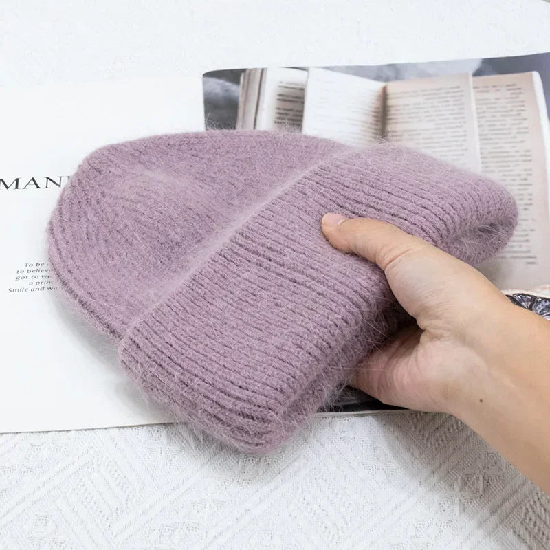 Un béret tricoté violet doux conçu comme un Bonnet Angora Pour Maman de BABY PREMA posé sur un magazine ouvert, avec une main posée doucement dessus pour afficher sa texture.