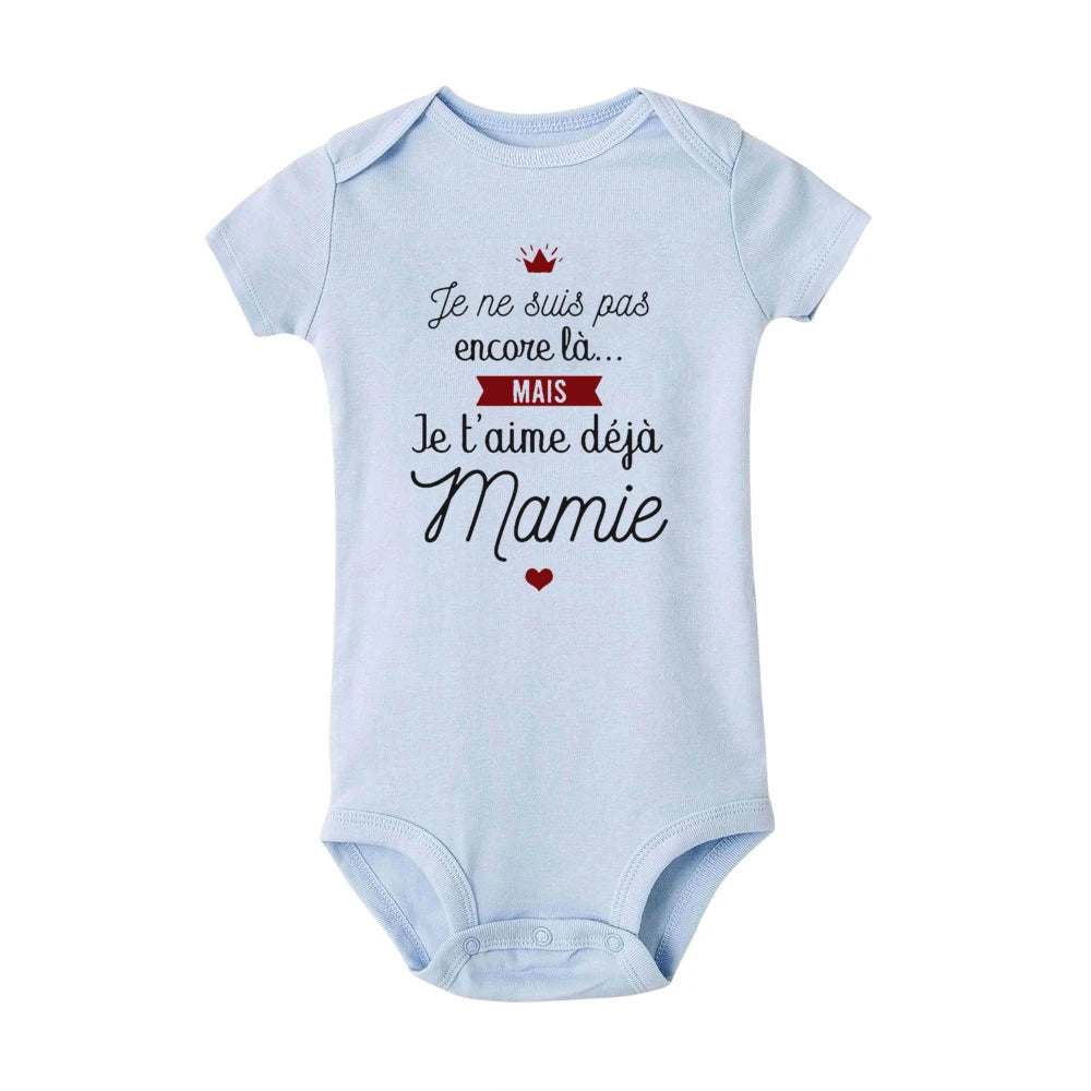 Une combinaison pour bébé Body Coton été Imprimé BABY-PREMA bleu clair avec le texte en français qui dit : « Je ne suis pas encore là... MAIS Je t'aime déjà Mamie » ainsi qu'un petit cœur rouge et une icône de couronne. Cette adorable pièce constitue un cadeau idéal grand-mère, se traduisant par "Je ne suis pas encore là... MAIS je t'aime déjà grand-mère.