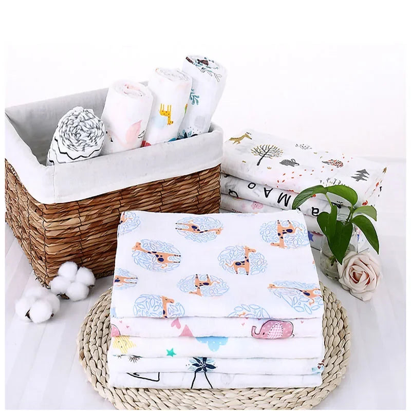 Un agencement soigné d'essentiels pour bébé comprenant des Langes en Mousseline en Coton pour Bébé pliés avec des motifs colorés, un panier en osier léger et un récipient de rangement gris doux, le tout sur un tapis circulaire tissé, accentué par un délicat BABY PREMA blanc.