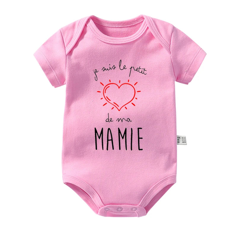 Body Rose Coton Manches Courtes de BABY-PREMA avec un motif cœur et le texte français "je suis le petit de ma mamie" en noir et rouge. Le body en coton possède une étiquette en tissu visible sur le côté, ce qui en fait un cadeau parfait pour bébé.