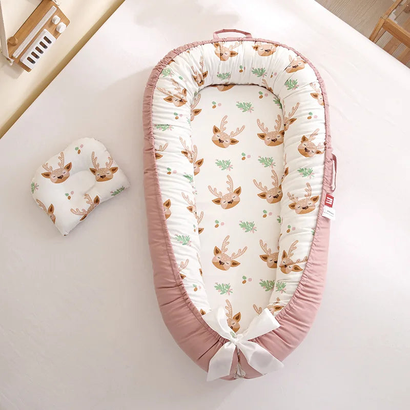 Une chaise longue pour bébé confortable avec un motif de cerf et des bords rose tendre, conçue pour une utilisation prématurée, complétée par un oreiller assorti, posé sur un fond clair pour une chambre de bébé sereine - le Lit de Bébé portable Nid de Cocoon de BABY-PREMA.