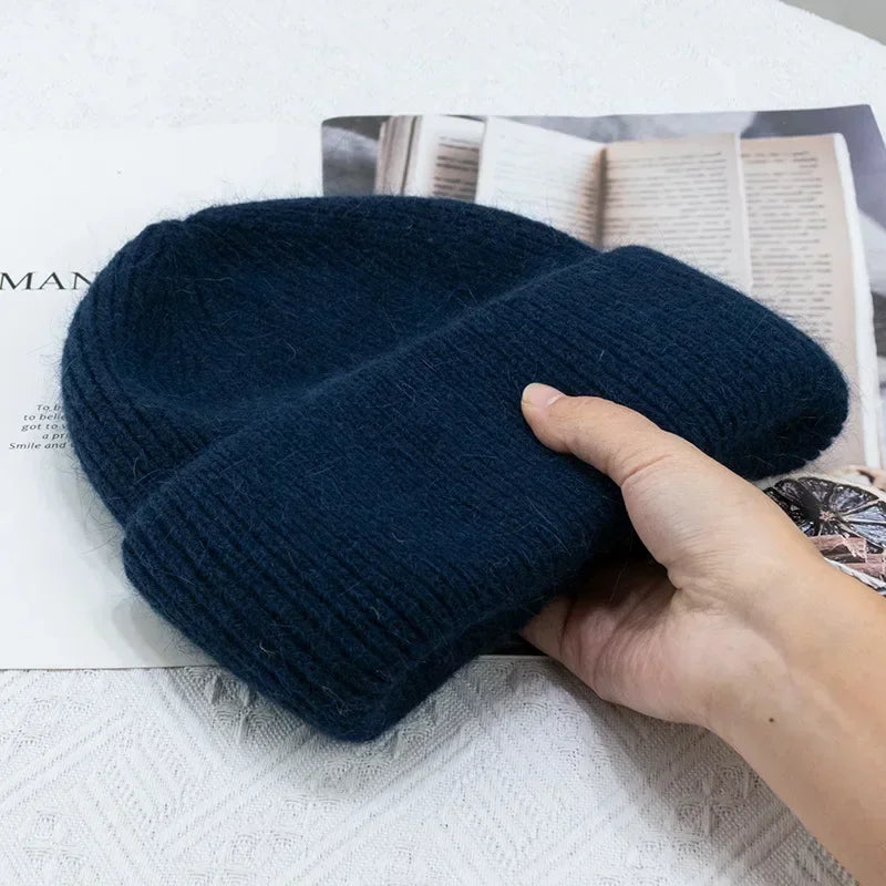 Une personne tenant un Bonnet Angora Pour Maman tricoté bleu marine foncé au-dessus d'un magazine ouvert.