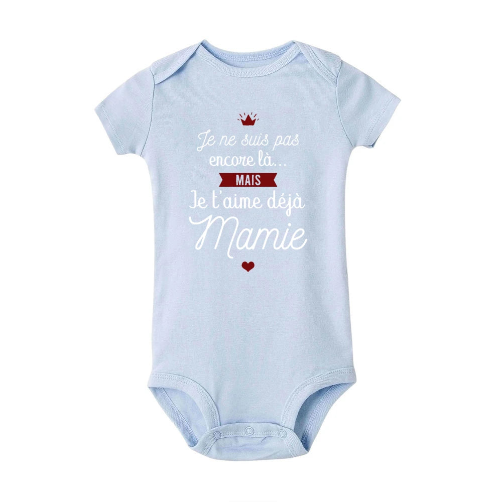 Body Coton été Imprimé bleu clair par BABY-PREMA, parfait comme cadeau grand-mère, comporte le texte en français qui dit : "Je ne suis pas encore là... MAIS Je t'aime déjà Mamie" avec un petit cœur rouge en dessous et une couronne rouge au-dessus du texte. Idéal pour un enfant en bas âge pendant les mois les plus chauds.