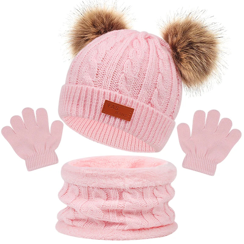 Un ensemble d'accessoires d'hiver rose composé du BABY PREMA Ensemble 3Pièces Bonnet Gants pour Bébé, qui comprend un bonnet tricoté avec deux pompons moelleux, une écharpe assortie et une paire de gants légers, présentés sur un fond blanc.