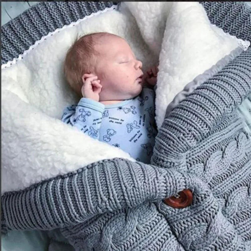 Un nouveau-né paisible dort confortablement enveloppé dans une douce couverture en polaire BABY PREMA grise ultra douce et moelleux avec une doublure en peluche blanche, respirant chaleur et confort, comprenant tout le nécessaire pour bébé pour garantir une hygiène ultime.