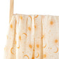 Un rideau de couleur crème au motif céleste, mettant en scène des soleils et des lunes dorés, suspendu à une tringle en bois sur fond blanc, parfait pour envelopper la Couverture Lange d'Emmaillotage de BABY PREMA dans l'espace dodo de bébé.