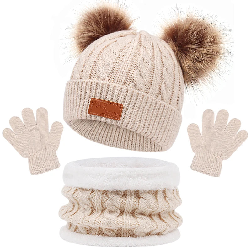 Un ensemble d'hiver douillet comprenant un bonnet tricoté beige avec deux pompons, une écharpe assortie et une paire de gants pour bébé du BABY PREMA Ensemble 3Pièces Bonnet Gants pour Bébé présentés sur un fond blanc.