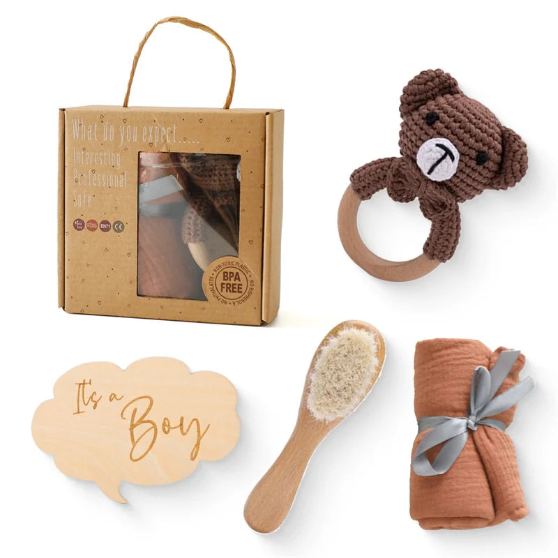 Une collection de cadeaux de baby shower comprenant un Coffret Cadeau Naissance Bébé de BABY PREMA, un hochet ours en peluche, une couverture bébé enveloppée, un faire-part "c'est un garçon" et d'autres accessoires.