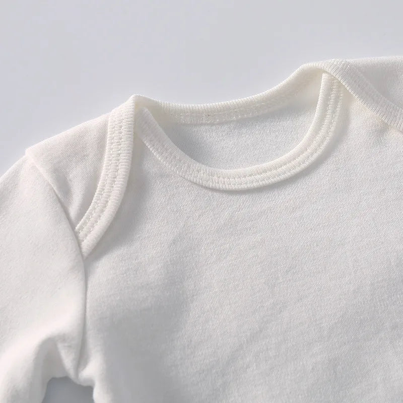 Photo en gros plan d'une combinaison pour bébé blanche unie en tissu de coton doux et léger. Le BABY-PREMA Body Noël Personnalisé pour Bébé, parfait pour se transformer en body de Noël personnalisé, présente un décolleté arrondi et s'affiche sur un fond blanc épuré.